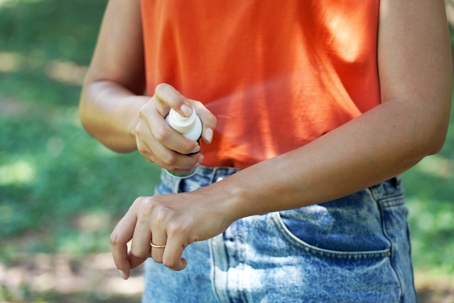 Girl spraying insect repellent on her arm outdoor.