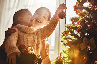 Mother and daughter decorating a Christmas tree with ornaments.